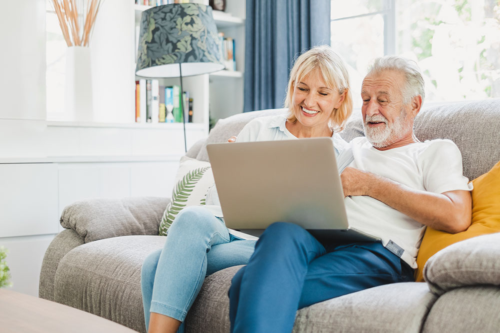 Senior couple with laptop on couch using internet