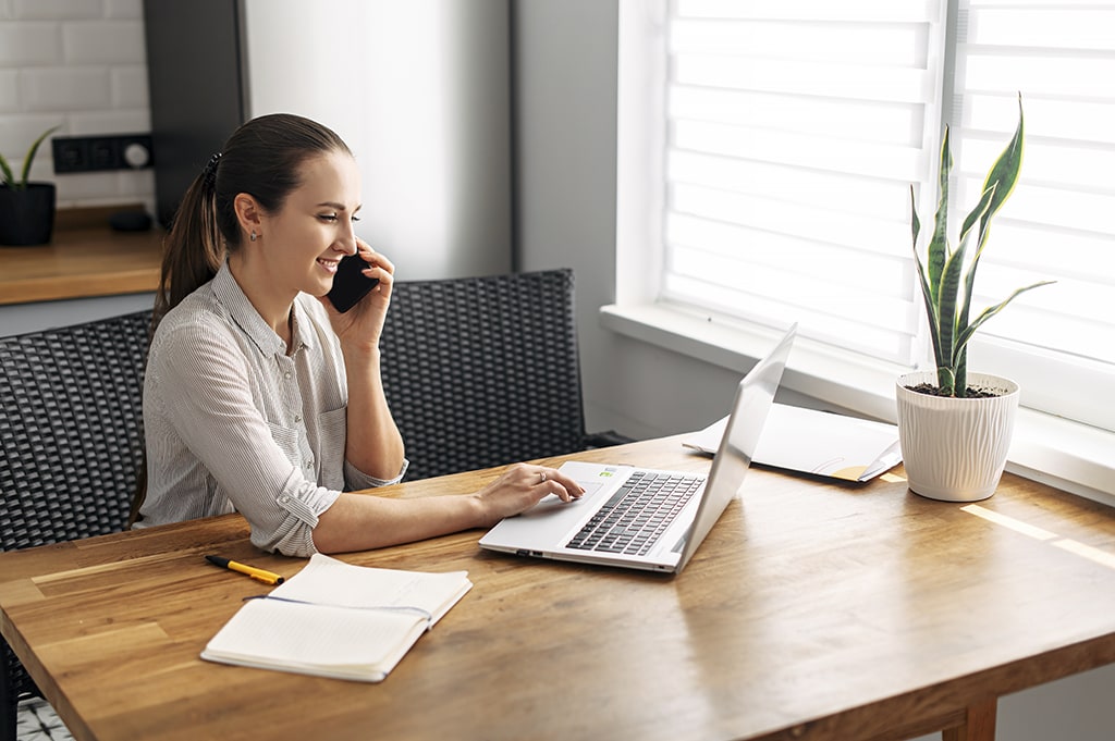 Young businesswoman talking on phone while working on laptop